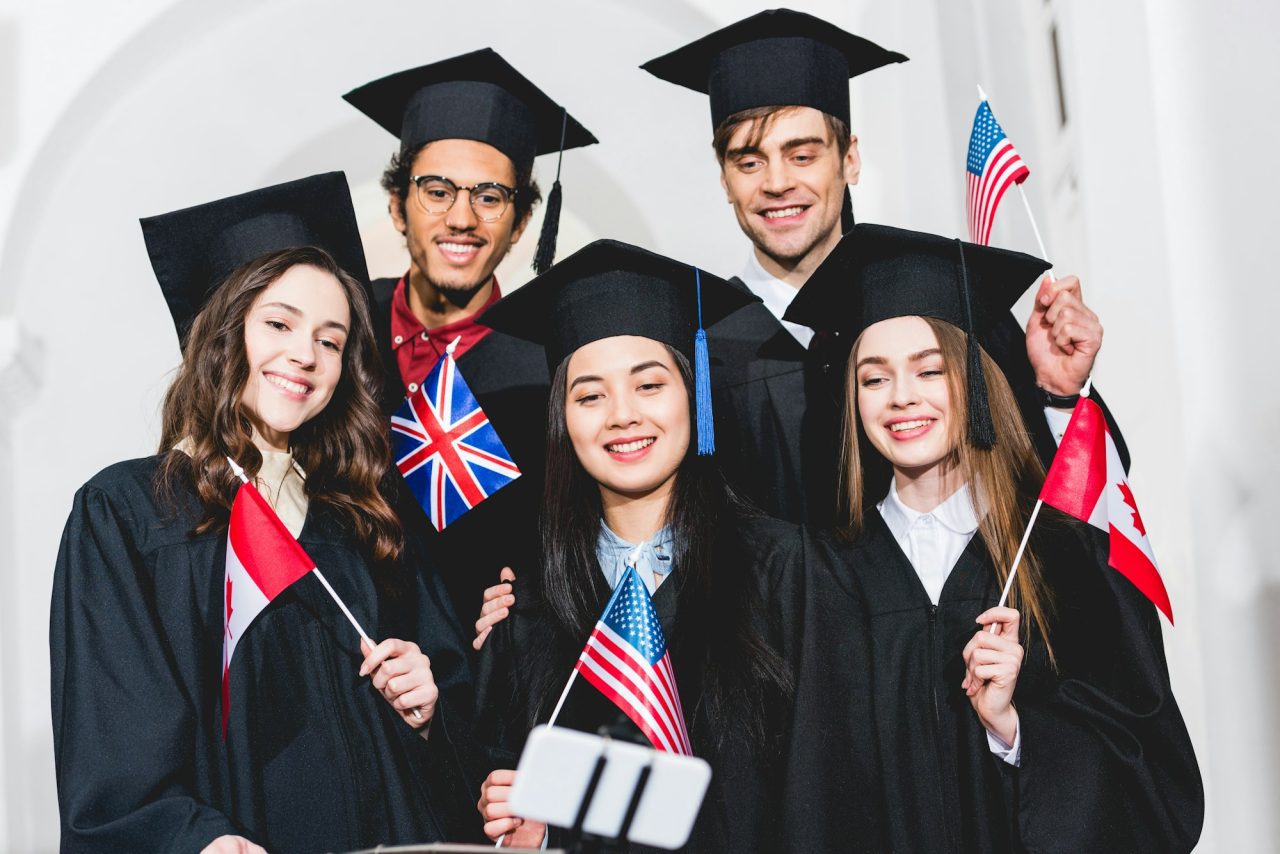 selective-focus-of-cheerful-students-in-graduation-gowns-holding-flags-of-different-countries-and.jpg